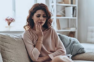 Woman holding her jaw while sitting on couch at home.
