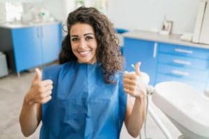 Woman smiling with thumbs up in dental office.