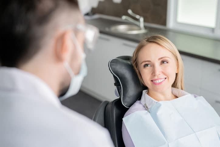 Happy young blonde female patient looking at her dentist with healthy smile while sitting in armchair before examination