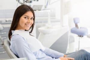 Pretty brunette female patient sitting on dentist chair and smiling at camera, free space