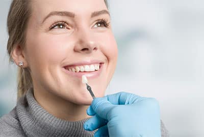 Woman Smiling with Dentist Holding Up a Dental Veneers in Birmingham MI