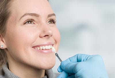 Brunette Woman Smiling with Dentist Holding Up a Dental Veneers in Michigan