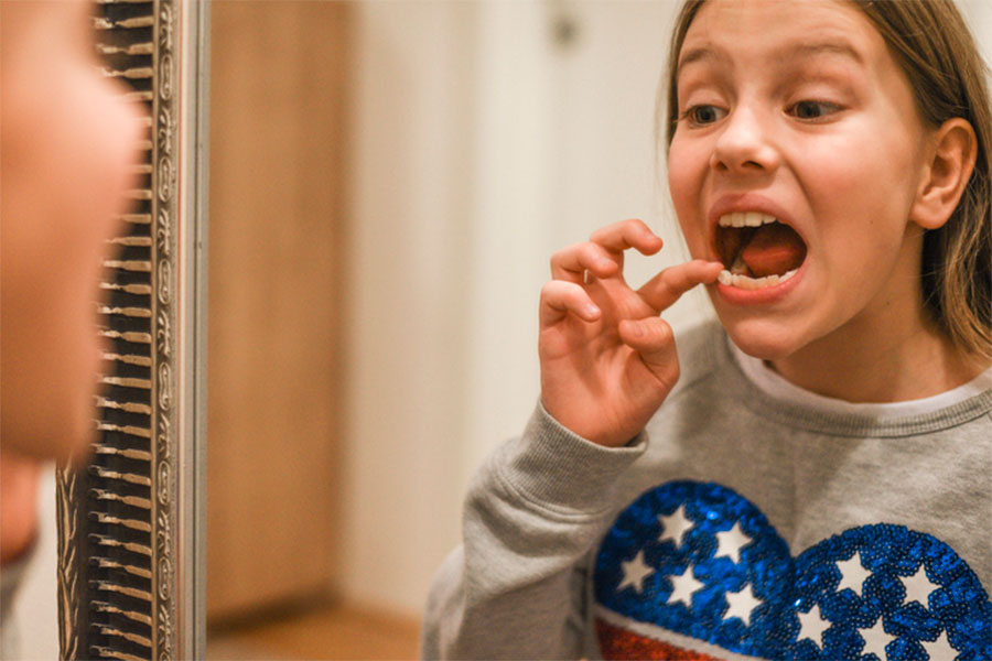 Girl looking in mirror at loose tooth.